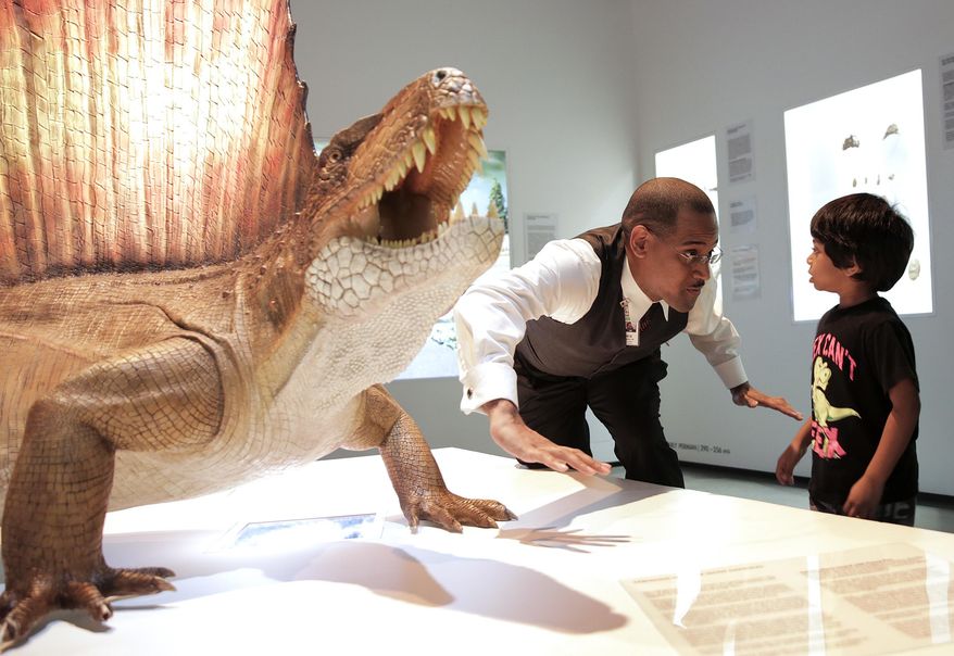 In a Tuesday, Dec. 6, 2016 photo, James Washington, the Houston Museum of Natural Science's most popular tour guide, demonstrates the difference between a lizard and a dinosaur to Ajay Selva, 4, during a tour of the museum, in Houston. Washington's tours are a blend of science, jokes and pop culture references. (Elizabeth Conley//Houston Chronicle via AP)