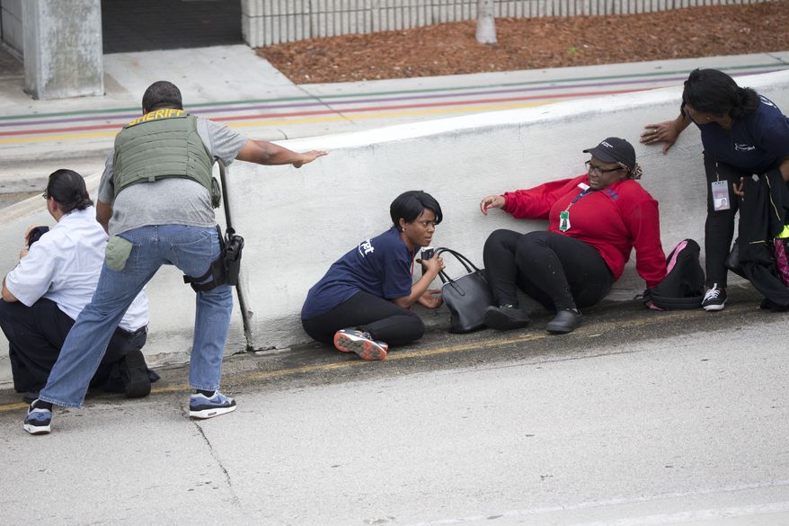 Law enforcement personnel tell people to take cover at Fort Lauderdale–Hollywood International Airport, Friday, Jan. 6, 2017, in Fort Lauderdale, Fla. A gunman opened fire in the baggage claim area at the airport Friday, killing several people and wounding others before being taken into custody in an attack that sent panicked passengers running out of the terminal and onto the tarmac, authorities said. (AP Photo/Wilfredo Lee)