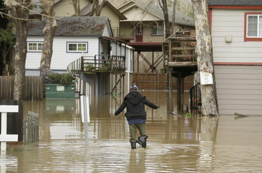 Melba Martinelli tries to keep her balance walking through flood water to her home Monday, Jan. 9, 2017, in Guerneville, Calif. A massive storm system stretching from California into Nevada lifted rivers climbing out of their banks, flooded vineyards and forced people to evacuate after warnings that hillsides parched by wildfires could give way to mudslides. (AP Photo/Eric Risberg)