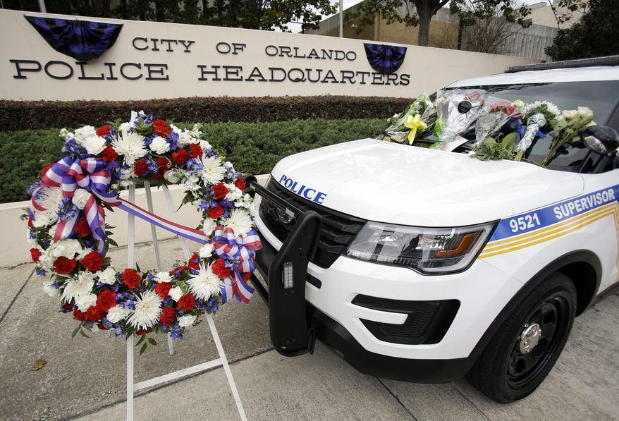 A wreath and flowers surround Orlando police shooting victim, officer Debra Clayton's patrol car, in front of police headquarters, Tuesday, Jan. 10, 2017, in Orlando, Fla. Clayton was killed Monday, and a manhunt continues as law enforcement officials search for the suspect. (AP Photo/John Raoux)