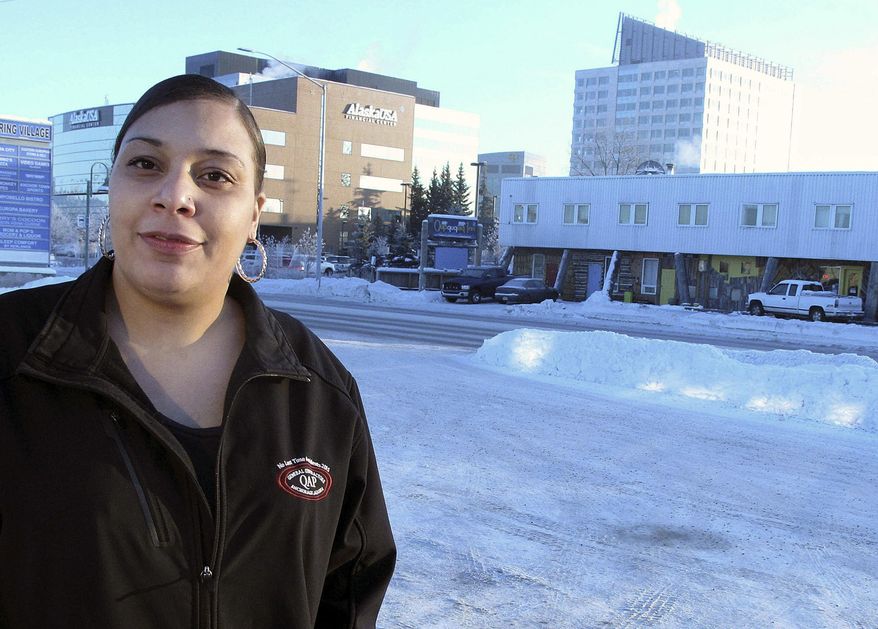 In this photo taken Tuesday, Jan. 10, 2017, Naomi Harden, a clerk at a local liquor and grocery store, is interviewed about waiting on alleged Fort Lauderdale shooter Esteban Santiago when he was staying across the street at the Qupqugiaq Inn, rear, in a gritty neighborhood in Anchorage, Alaska. Harden said she witnessed Santiago screaming and waving his arms in the parking lot of the store. (AP Photo/Rachel D'Oro)