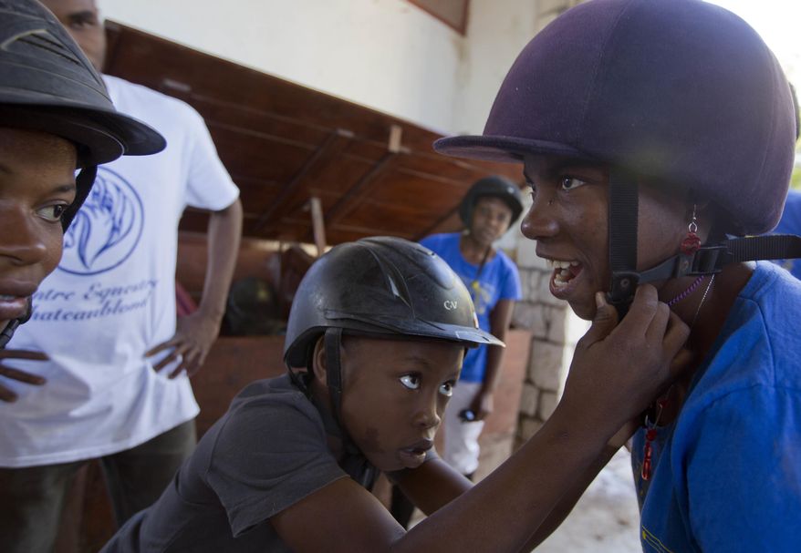 In this Jan. 11, 2017 photo, Judeley Hans Debel helps his friend Fabienne Charles with her helmet at the Chateaublond Equestrian Center in Petion-Ville, Haiti. Both are receiving free, therapeutic horse riding lessons at the center, which advocates say provides muscle and nerve stimulation to disabled youngsters. (AP Photo/Dieu Nalio Chery)