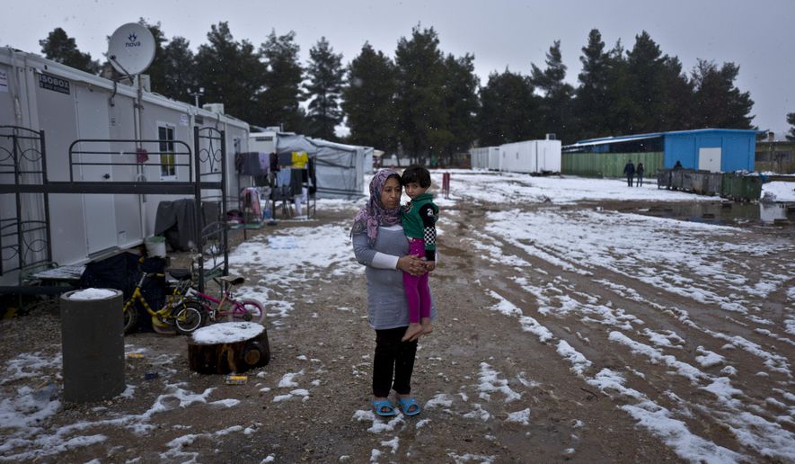 In this Friday, Dec. 30, 2016 photo, Maha Abdulqadir, age 30 and 3 months pregnant, a Syrian refugee from al-Hasaka, holds her daughter Zinnar, 5, while posing for a picture by the entrance of her shelter, during snowfall at the refugee camp of Ritsona, Greece. "We fled from war, nothing left for us in Syria, I miss my home everything was taken from us, now in Greece we are on hold without any knowledge of what is next.", Abdulqadir said. Squalid conditions and subfreezing temperatures in Greece’s migrant camps this winter are taking their toll on everyone living in them with expectant mothers and babies especially feel the brunt. (AP Photo/Muhammed Muheisen)