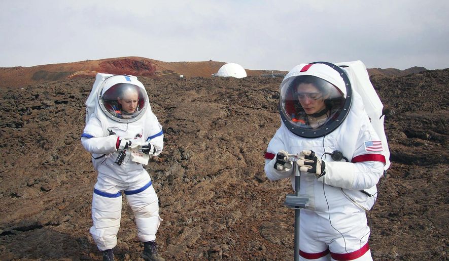 In this May 23, 2014 photo provided by the University of Hawaii, Lucie Poulet, right, uses a geotechnical tool while Annie Caraccio records the data during a previous study outside the domed structure that will house six researchers for eight months in an environment meant to simulate an expedition to Mars, on Mauna Loa on the Big Island of Hawaii. The group will enter the dome Thursday, Jan. 19, 2017, and spend eight months together in the 1,200-square-foot research facility in a study called Hawaii Space Exploration Analog and Simulation (HI-SEAS). They will have no physical contact with any humans outside their group, experience a 20-minute delay in communications and are required to wear space suits whenever they leave the compound. (Ross Lockwood/University of Hawaii via AP)