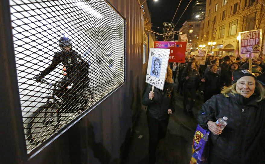 A Seattle Police officer on a bicycle eyes protesters taking part in a protest against President Donald Trump as he rides through construction walkway, Friday, Jan. 20, 2017, in Seattle. (AP Photo/Ted S. Warren)