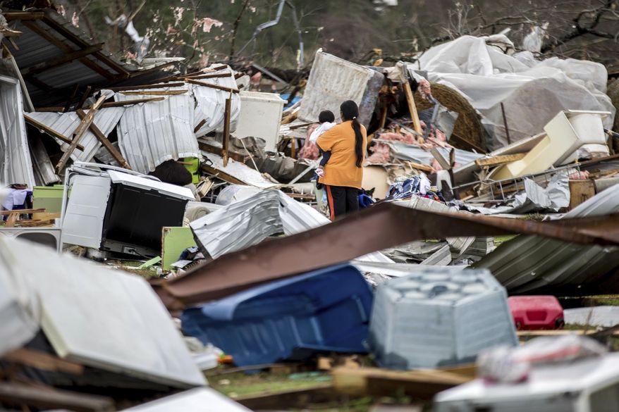A woman holds a child while walking through a farm that was damaged by a tornado, Sunday, Jan. 22, 2017, in Adel, Ga. (AP Photo/Branden Camp)
