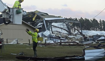 Sumter Utilities worker Cole Eubanks throw a part up to co-worker Kenny Morgan in front of the remains of a Valdosta Plant Co. building Sunday, Jan. 22, 2017, in Adel, Ga. Emergency responders rushed to answer new reports of deaths and injuries Sunday evening in southern Georgia as violent storms already blamed for killing more than a dozen of people in the Southeast continued to inflict destruction. (AP Photo/Phil Sears)