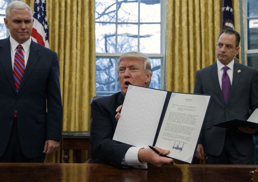 Vice President Mike Pence, left, and White House Chief of Staff Reince Priebus, right, watch as President Donald Trump shows off an executive order to withdraw the U.S. from the 12-nation Trans-Pacific Partnership trade pact agreed to under the Obama administration in the Oval Office of the White House in Washington on Jan. 23, 2017. (Associated Press)