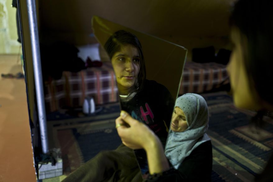 In this Tuesday, Jan. 17, 2017 photo, Syrian refugee Kulnawaz Youssef, 13, looks at herself in a mirror at her tent in Kalochori refugee camp on the outskirts of the northern Greek city of Thessaloniki. Many migrants living in this warehouse tent camp and another one nearby are feeling burned out. They try to keep busy as they dream of a better life in Western Europe and not let boredom or depression set in. (AP Photo/Muhammed Muheisen)