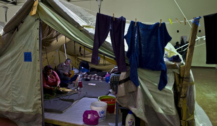 In this Tuesday, Jan. 17, 2017 photo, a Syrian refugee woman cuts vegetables while her husband checks his mobile phone at their tent in Kalochori refugee camp on the outskirts of the northern Greek city of Thessaloniki. (AP Photo/Muhammed Muheisen)