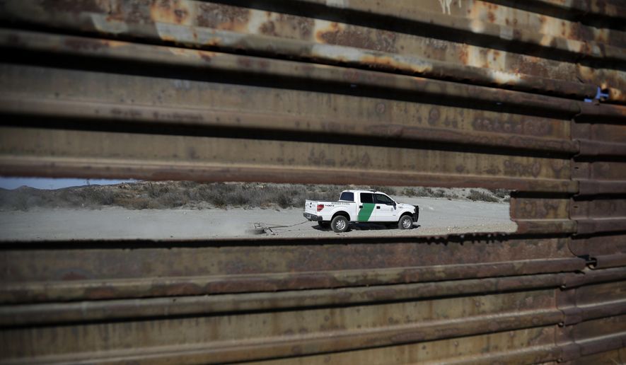 In this Nov. 9, 2016, file photo, a Border Patrol vehicle drives by in Tecate, Calif., seen through a hole in the metal barrier that lines the border in Tecate, Mexico. U.S. President Donald Trump will direct the Homeland Security Department to start building a wall at the Mexican border. (AP Photo/Gregory Bull, file)