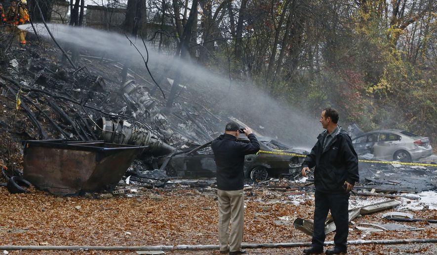 FILE - In a Tuesday, Nov. 10, 2015 file photo, Terry Ellis, left, takes photos as firefighters work at the scene where authorities say a small business jet crashed into an apartment building in Akron, Ohio. A second lawsuit has been filed seeking damages over the deadly crash of a corporate jet into the Ohio apartment building. The Akron Beacon Journal reports a resident of an apartment destroyed in the 2015 crash is suing the Florida company that owned the plane and the estates of the two pilots who died. (Ed Suba Jr./Akron Beacon Journal via AP, File)