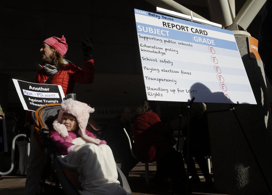Miriam Haskey, 4, sits in her stroller next to a report card placard as she attends a rally with her mother, Cara Haskey, in Portland, Ore., Friday, Jan. 27, 2017. Several hundred supporters gathered with Oregon congressional leaders in protest against Education Secretary nominee Betsy DeVos. (AP Photo/Don Ryan)