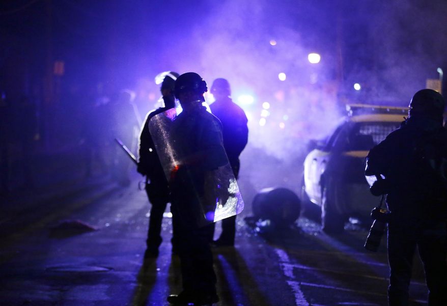 FILE - In this Nov. 25, 2014 file photo, police officers watch protesters as smoke fills the streets in Ferguson, Mo. Clark Ervin, a Washington lawyer monitoring the consent decree involving the St. Louis suburb that has been under Justice Department scrutiny since the fatal 2014 police shooting of Michael Brown, said Ferguson missed deadlines in crafting new policies and procedures on basic policing practices. (AP Photo/Charlie Riedel, File)