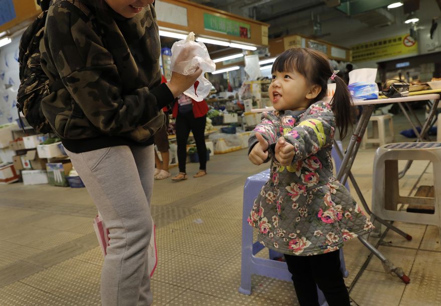 In this Monday, Jan. 23, 2017 photo, a girl reacts after tasting a chicken feet at a snacks shop in Hong Kong. Saturday marks the start of the lunar Year of the Rooster and families in China will reunite for festivities, fireworks and food. While tradition calls for feasting on “auspicious” foods, many will also munch on staple snacks like “phoenix claws,” the Chinese name for chicken feet. (AP Photo/Vincent Yu)
