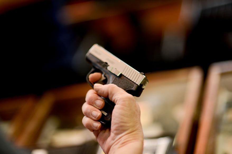a woman holds a small pistol at the Annapolis Gun Show, Annapolis, Md., Sunday, April 14, 2013. (Andrew Harnik/The Washington Times)