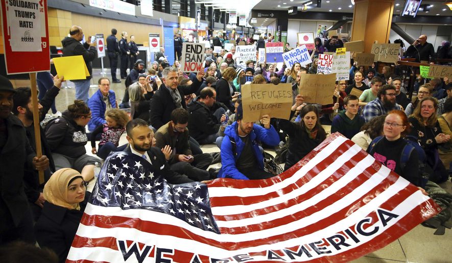 Demonstrators sit down in the concourse and hold a sign that reads &amp;quot;We are America,&amp;quot; as more than 1,000 people gather at Seattle-Tacoma International Airport, to protest President Donald Trump&#39;s order that restricts immigration to the U.S., Saturday, Jan. 28, 2017, in Seattle. President Trump signed an executive order Friday that bans legal U.S. residents and visa-holders from seven Muslim-majority nations from entering the U.S. for 90 days and puts an indefinite hold on a program resettling Syrian refugees. (Genna Martin/seattlepi.com via AP)