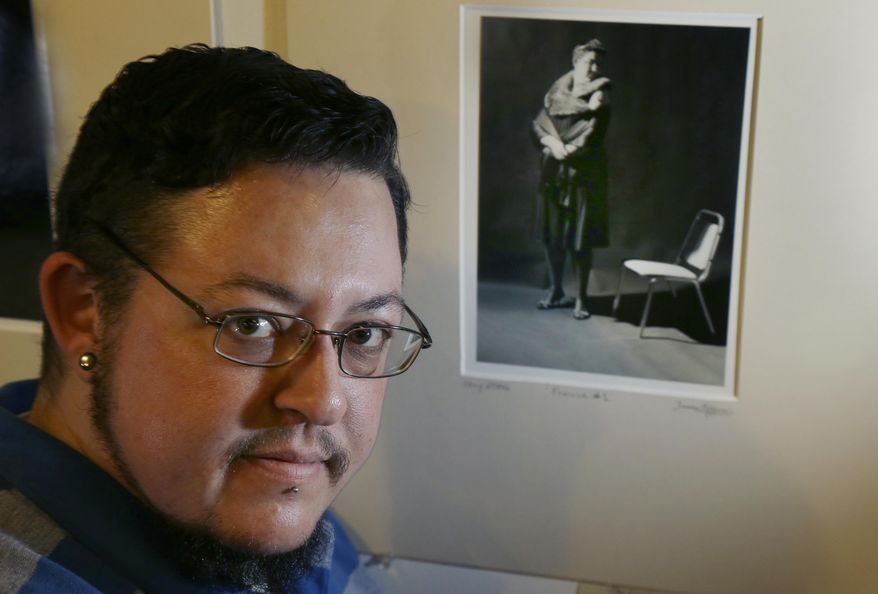 In this Jan. 25, 2017 photo, artist Jeff Kramer poses next to one of his self-portraits entitled "The Gender Series," a part of the group exhibit "This is What TRANS Feels Like" at Wrong Brain Art Collective in Dover, N.H. Kramer said he wants people to see that gender is based on a spectrum and that roles keep changing. The exhibit runs through Feb. 14. (AP Photo/Elise Amendola)