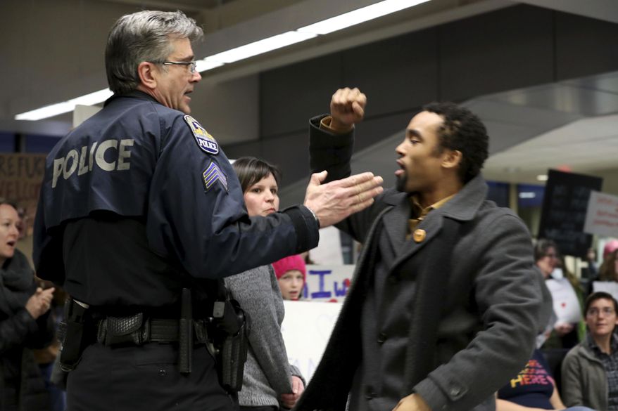 James Badue, who is with the Minnesota NAACP, leads other opponents in a chant: "No hate, no fear, immigrants are welcome here," as an airport police officer tries to quiet him, at the Minneapolis-St. Paul International Airport, Saturday, Jan. 28, 2017, in Minneapolis. Protesters were responding to an executive order signed by President Donald Trump, restricting immigration from several Muslim nations. (David Joles/Star Tribune via AP)