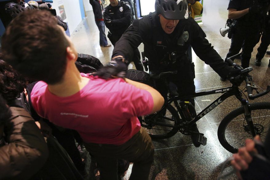 A Seattle police officer pushes the last group of protesters out of the airport terminal after giving a final dispersal order around 2:00 a.m. Sunday, Jan. 29, 2017 as about 3,000 people gather at Seattle-Tacoma International Airport in Seattle to protest President Donald Trump's order that restricts immigration to the U.S. Trump signed an executive order Friday that bans legal U.S. residents and visa-holders from seven Muslim-majority nations from entering the U.S. for 90 days and puts an indefinite hold on a program resettling Syrian refugees. (Genna Martin/seattlepi.com via AP)