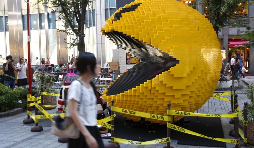 FILE - In this Aug. 12, 2015, file photo, a woman walks past a three-meter (nine-foot)-tall Pac-Man made of Lego bricks, in Tokyo's Shinjuku area. Masaya Nakamura, the "Father of Pac-Man" who founded the Japanese video game company behind the hit creature-gobbling game, has died on Jan. 22, 2017, at age 91, the company Bandai Namco said. (AP Photo/Ken Aragaki, File)