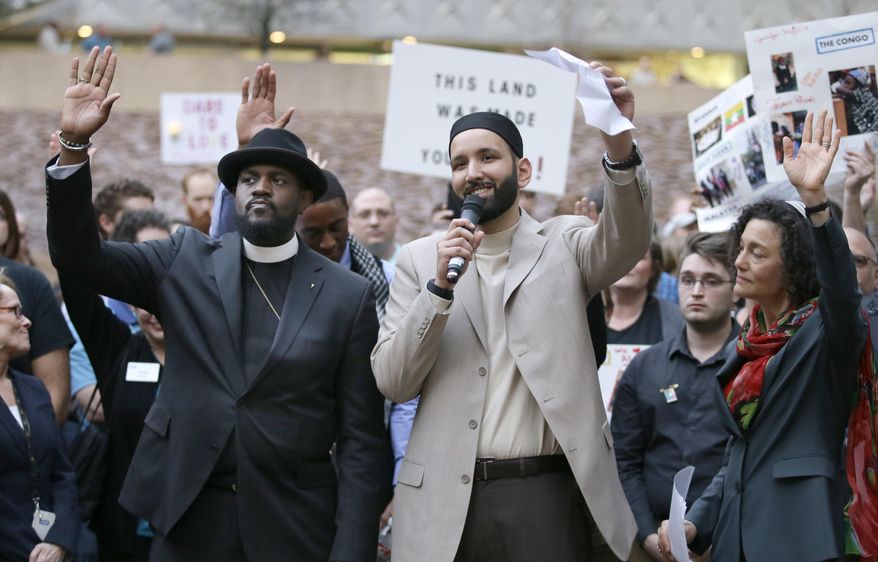 Iman Omar Suleiman, center, raises his hand with Rabbi Nancy Kasten, right, and the Rev. Michael W. Waters while speaking before a candlelight vigil at Thanksgiving Square in downtown Dallas, Monday, Jan. 30, 2017. Community activist gathered to protest against President Donald Trump's executive order temporarily banning immigrants from seven Muslim-majority countries from entering the U.S. and suspending the nation’s refugee program. (AP Photo/LM Otero)