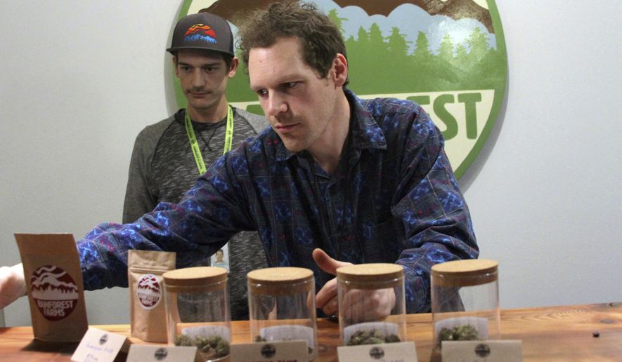 In this Jan. 18, 2017 photo shows Giono Barrett, right, arranges marijuana products at Rainforest Farms in Juneau, Alaska. James Barrett, left, is co-owner of Juneau's first marijuana retail store. James and Giono Barrett have a dream: that some of the scores of cruise ship passengers who crowd the streets of the state capital each summer will one day use their shore excursions to kick back and light up a joint in a pot store's lounge. (AP Photo/Mark Thiessen)