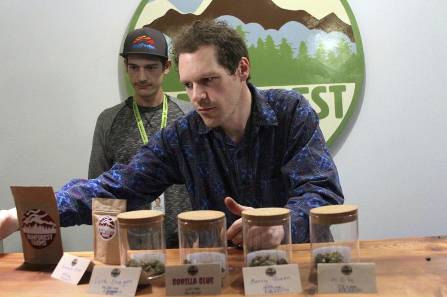 In this Jan. 18, 2017 photo shows Giono Barrett, right, arranges marijuana products at Rainforest Farms in Juneau, Alaska. James Barrett, left, is co-owner of Juneau's first marijuana retail store. James and Giono Barrett have a dream: that some of the scores of cruise ship passengers who crowd the streets of the state capital each summer will one day use their shore excursions to kick back and light up a joint in a pot store's lounge. (AP Photo/Mark Thiessen)