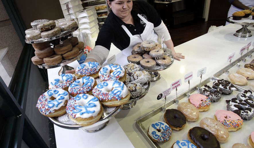 In this Jan. 30, 2017 photo, Katie Hayward places a tray of "Go Pats" donuts on display at Kane's Donuts in Boston. Kane's Donuts of Saugus/Boston and Atlanta's Sublime Doughnuts are wagering a dozen of their respective handcrafted donuts on the outcome of the New England Patriots vs. Atlanta Falcons NFL Super Bowl football game on Sunday. (AP Photo/Elise Amendola)