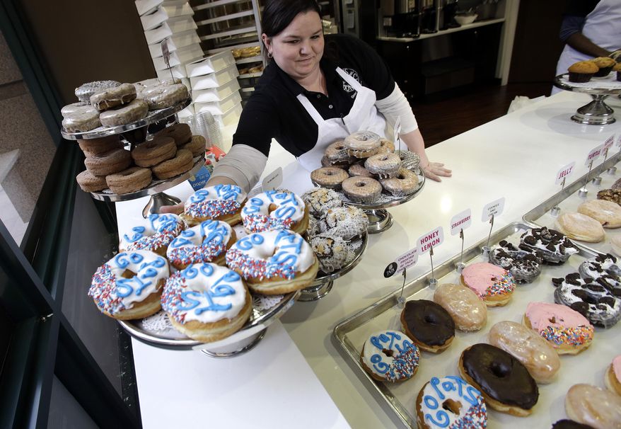 In this Jan. 30, 2017 photo, Katie Hayward places a tray of "Go Pats" donuts on display at Kane's Donuts in Boston. Kane's Donuts of Saugus/Boston and Atlanta's Sublime Doughnuts are wagering a dozen of their respective handcrafted donuts on the outcome of the New England Patriots vs. Atlanta Falcons NFL Super Bowl football game on Sunday. (AP Photo/Elise Amendola)