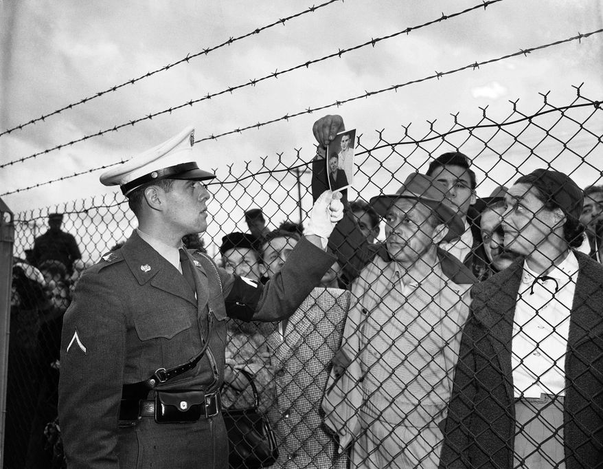 FILE - In this Nov. 21, 1951 file photo, Bill Vetesy of Colonia, N.J., holds a picture of his mother and brother as he asks a military police officer inside the fence at Camp Kilmer, N.J., if they are among the 60 Hungarian refugees who arrived at the camp. The first plane load of refugees arrived at nearby McGuire Air Force Base from Vienna earlier in the day. The refugees will be housed at Camp Kilmer until quarters in private homes are made available to them in the United States. (AP Photo/Anthoy Camerano, File)