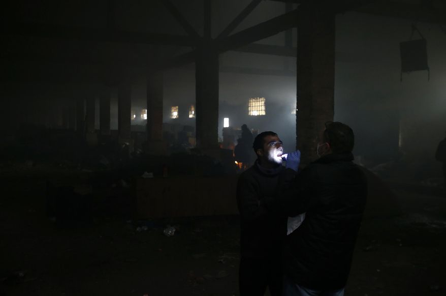 Doctor Yaser Harawi, right, checks the throat of a migrant in an abandoned warehouse in Belgrade, Serbia, Saturday, Jan. 28, 2017. Harawi, who has lived in Serbia for over thirty years, has found meaning in helping Syrian and other migrants passing through the Balkan country in search of a better future in Western Europe. (AP Photo/Darko Vojinovic)