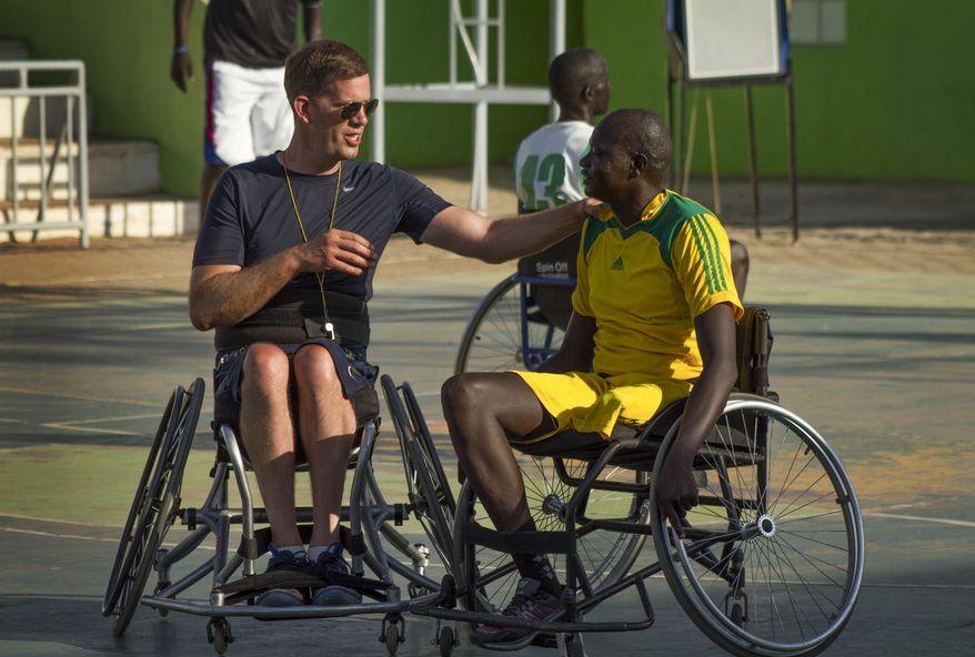 In this photo taken Friday, Jan. 20, 2017, wheelchair basketball coach Jess Markt from Colorado, left, chats with a player during a tournament in Juba, South Sudan. Warnings of possible genocide hang over the world's youngest nation, but here on a basketball court under a fierce morning sun, South Sudan's civil war seems like another country. (AP Photo/Bullen Chol)