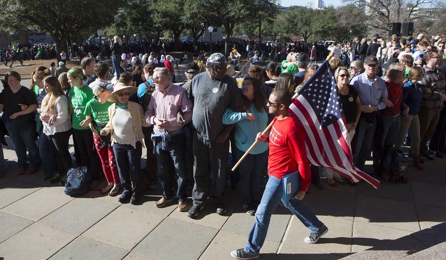 Ahmed El Shenawy carries the American Flag around a wall of humans intended to protect the stage on the steps of the capitol for Texas Muslim Capitol Day, Tuesday, Jan. 31, 2017, at the Texas Capitol in Austin, Texas. (AP Photo/Stephen Spillman)