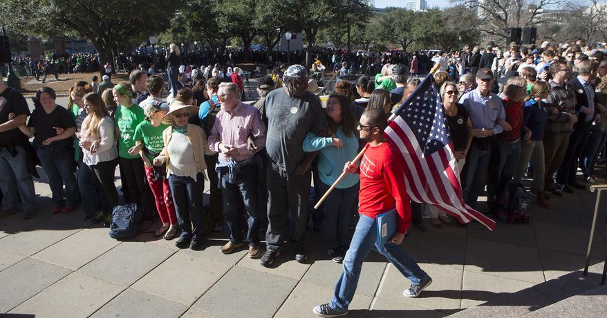 Ahmed El Shenawy carries the American Flag around a wall of humans intended to protect the stage on the steps of the capitol for Texas Muslim Capitol Day, Tuesday, Jan. 31, 2017, at the Texas Capitol in Austin, Texas. (AP Photo/Stephen Spillman)