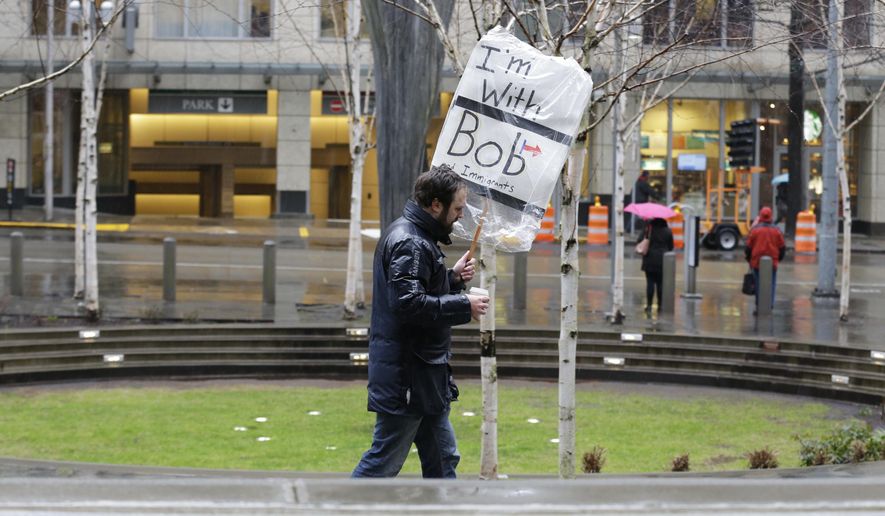 A person walks outside the federal courthouse in Seattle carrying a sign that reads "I'm with Bob and Immigrants," in reference to Washington state Attorney General Bob Ferguson, Friday, Feb. 3, 2017, during a hearing in federal court. A U.S. judge on Friday temporarily blocked President Donald Trump's ban on people from seven predominantly Muslim countries from entering the United States after Washington state and Minnesota urged a nationwide hold on the executive order that has launched legal battles across the country. (AP Photo/Ted S. Warren)