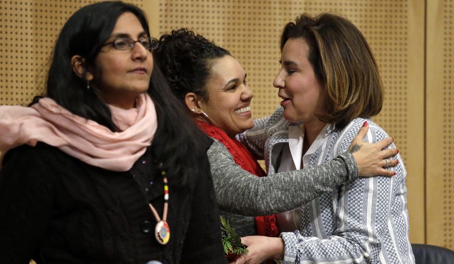 Seattle City Council member Debora Juarez, right, is embraced by Rachel Heaton, a Muckleshoot tribal member, as Council member Kshama Sawant stands nearby after Heaton gave both women gifts from the Native American community before a Council meeting Tuesday, Feb. 7, 2017, in Seattle. The City Council is scheduled to vote on whether to divest $3 billion in city funds from Wells Fargo over its funding of the Dakota Access Pipeline. (AP Photo/Elaine Thompson)
