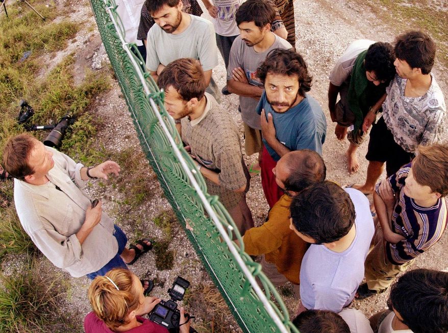 FILE - In this Sept. 19, 2001, file photo, refugees, right, gather on one side of a fence to talk with international journalists about their journey that brought them to the Island of Nauru. U.S. officials had stopped screening refugees for potential resettlement in the United States but would return to the Pacific atoll of Nauru to continue working toward a deal that President Donald Trump has condemned as "dumb,” an Australian minister said on Thursday. (AP Photo/Rick Rycroft, File)