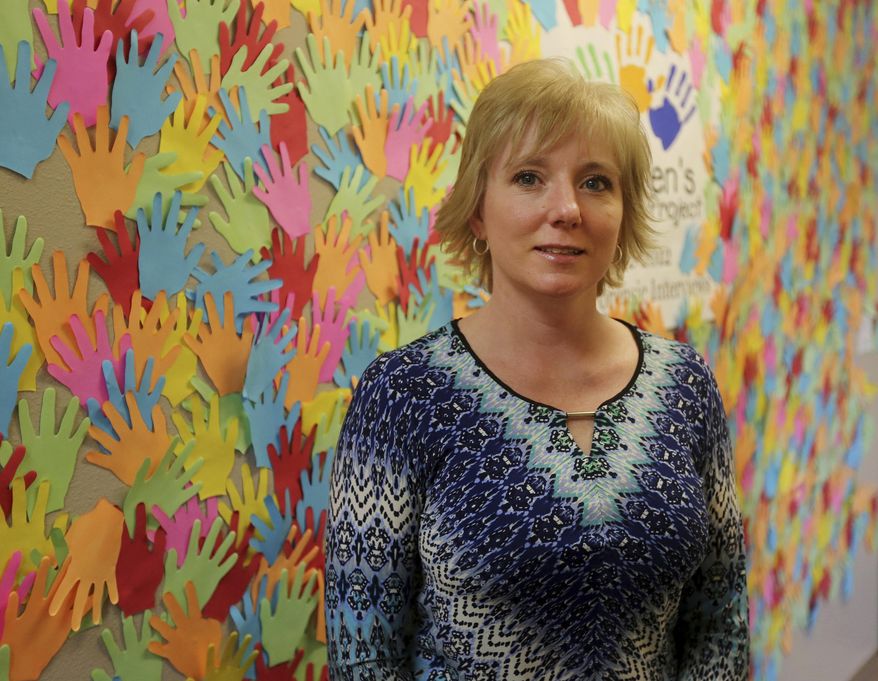 Executive director Stacy Nelson poses in front of a wall covered in hands representing the children the organization has helped over the years on Jan. 23, 2017 at the Children's Advocacy Project in Casper, Wyo. Three child advocacy facilities have seen their funding change repeatedly over the past few years as state agencies were asked to slash expenses. (Dan Cepeda, Casper Star-Tribune via AP)