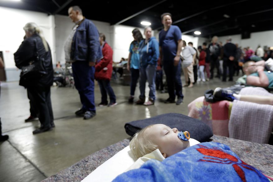 Jace Lawson, 1, of Oroville, Calif., bottom, sleeps as people behind wait for a meal at a shelter for evacuees from city's surrounding the Oroville Dam, Monday, Feb. 13, 2017, in Chico, Calif. The thousands of people who were ordered to leave their homes after a damaged California spillway threatened to unleash a 30-foot wall of water may not be able to return until significant erosion is repaired, authorities said Monday. (AP Photo/Marcio Jose Sanchez)