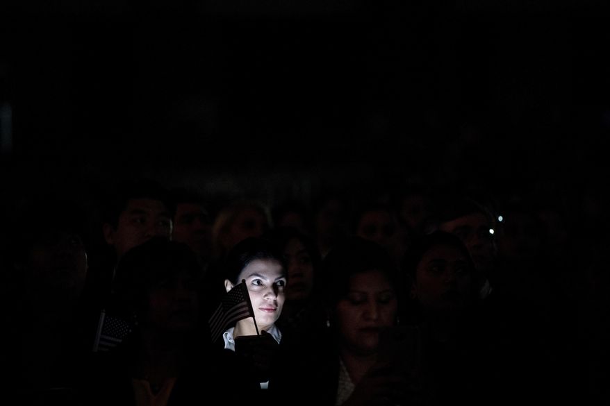 Armenian immigrant Naira Hallabyan is lit by her smartphone screen while watching a video presentation during a naturalization ceremony at the Los Angeles Convention Center, Wednesday, Feb. 15, 2017, in Los Angeles. About 3,000 people took the oath in the morning and more than 3,500 others were expected during an afternoon ceremony, according to U.S. Citizenship and Immigration Services officials. (AP Photo/Jae C. Hong)