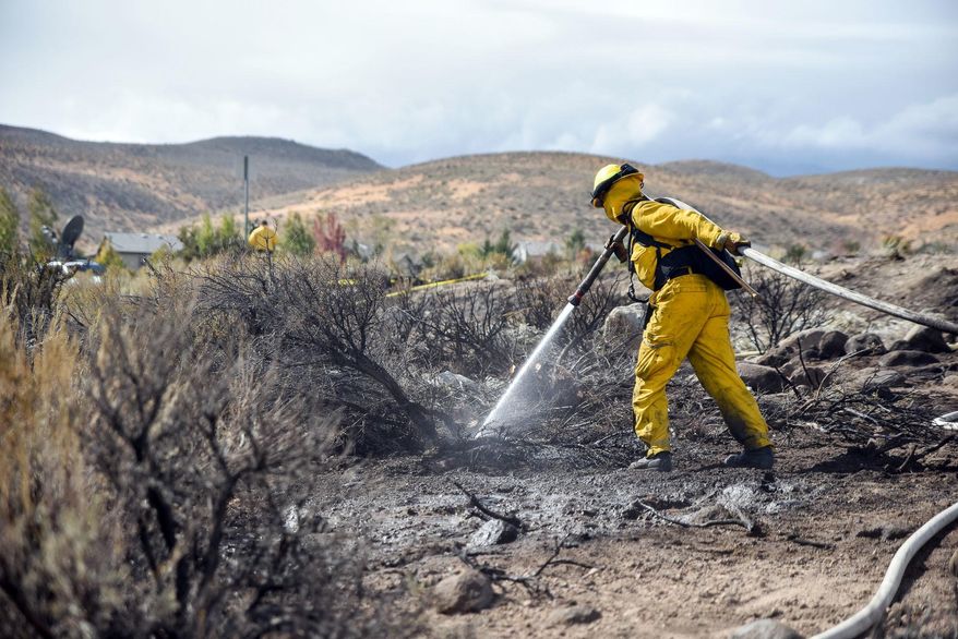 FILE - In this Oct. 14, 2016, file photo, a firefighter hoses down the area on Mount Rose Highway and Edmonton Drive in Reno, Nev. An investigation into a prescribed burn that sparked a northern Nevada wildfire that destroyed 23 homes found several questionable practices on the part of the Nevada Division of Forestry, including understaffing despite an understanding that unstable weather conditions made for a potentially dangerous situation.(Mike Higdon/The Reno Gazette-Journal via AP, File)