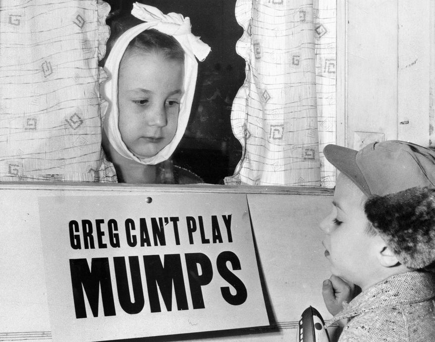 FILE - In this Jan. 16, 1957 file photo, Jon Douglas, 6, right, visits his friend, Greg Cox, standing behind a sign warning he has mumps, on the door of his home in Altamont, Ill. Fifty years ago, mumps was once a childhood rite of passage of puffy cheeks and swollen jaws. That all changed with the arrival of a vaccine in the late 1960s, and mumps nearly disappeared. But in 2017, the U.S. is in the midst of one of the largest surges in decades. (AP Photo)