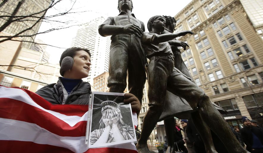 Molly Hitt, of Boston, displays an American flag while standing in front of a memorial to the Irish potato famine, right, during a rally called "We Will Persist," Tuesday, Feb. 21, 2017, in Boston. According to organizers the rally was held to send a message to Republicans in Congress and the administration of President Donald Trump that they will continue to press for immigration rights and continued affordable healthcare coverage. (AP Photo/Steven Senne)