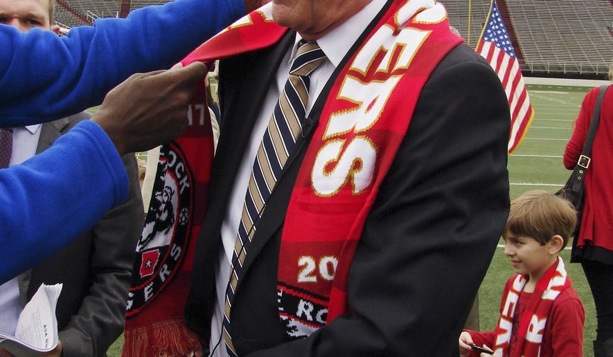 A television cameraman adjusts a scarf as he reaches in to place a microphone on Gov. Asa Hutchinson as the governor prepares to talk to reporters Wednesday, Feb. 22, 2017, about bills in the Arkansas Legislature that would impose taxes on online purchases. Hutchinson, who had just been given a scarf from the Little Rock Rangers soccer team, spoke on the floor of War Memorial Stadium in Little Rock. (AP Photo/Kelly P. Kissel)