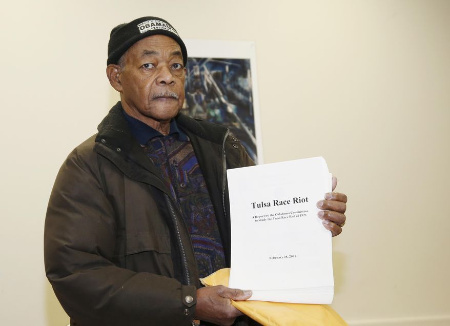 In this Thursday, Dec. 15, 2016 photo, Ralph Knight poses with a copy of a report on the Tulsa Race Riot, during an interview in Tulsa, Okla. Knight, a retired airline mechanic whose mother was 6 when the rioting began, said a turnaround could remedy some of the blight that now pocks the community and give a younger generation reason to hope, and stay, in north Tulsa. (AP Photo/Sue Ogrocki)