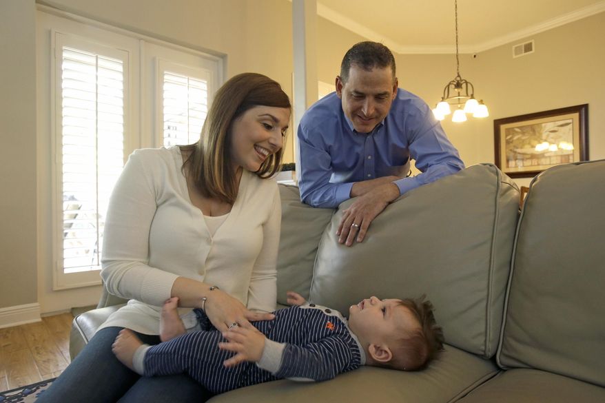 In this Tuesday, Feb. 7, 2017 photo, Lauren Nieves-Taranto, left, and husband Francisco play with their youngest child Nicolas, 4-months, at their home in Windermere, Fla. Nieves-Taranto covered the entire $8,000 bill from the birth of Nicolas last year with his account balance from a health savings account, or HSA. (AP Photo/John Raoux)