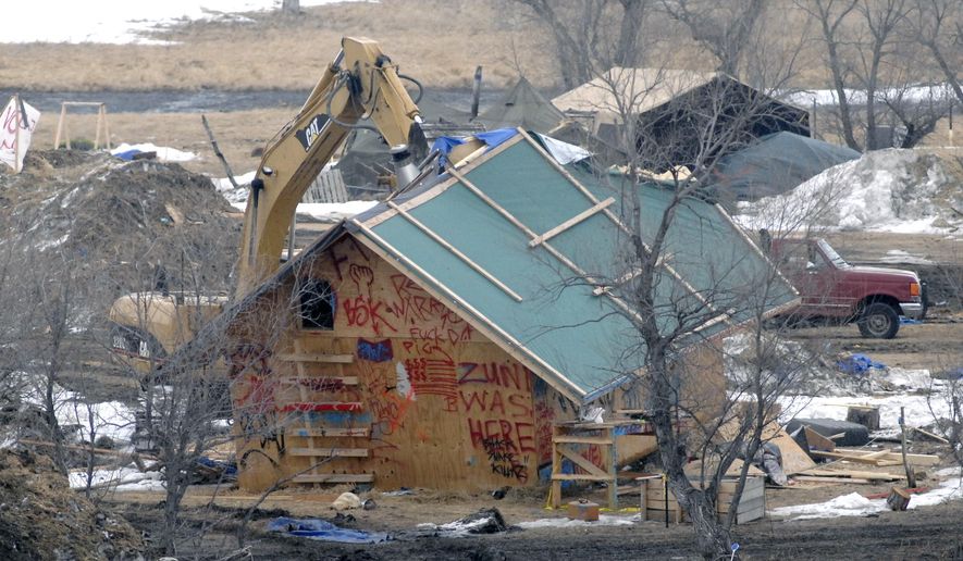 A backhoe rips through a wood structure to begin the cleaning up process at the Oceti Sakowin camp as law enforcement swept through the camp arresting the final Dakota Access oil pipeline protesters in Morton County Thursday, Feb. 23, 2017, near Cannon Ball, N.D. (Mike McCleary/The Bismarck Tribune via AP, Pool)