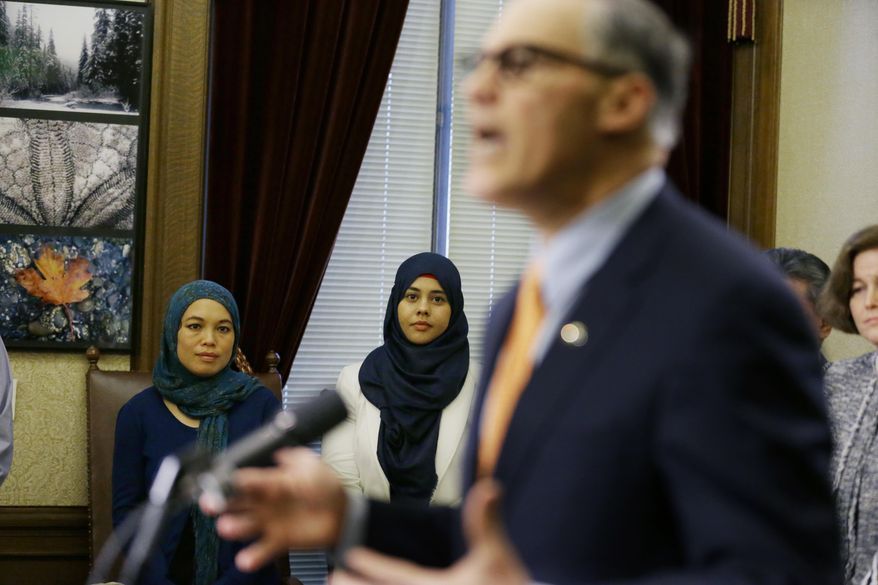 Rokaih Vansot, left, a member of the Washington state chapter of the Council on American-Islamic Relations, stands with Aishah Bomani, center, the principal of Seattle's Makkah Islamic School, as they listen to Washington Gov. Jay Inslee, right, talk to reporters, Thursday, Feb. 23, 2017, at the Capitol in Olympia, Wash., after Inslee signed an executive order to ensure that state workers don't help carry out President Donald Trump's immigration policies. Trump has said he wants to expand the number of deportations of people in the country illegally, and Inslee said Thursday that his order reaffirms the state's commitment to tolerance and ensures that state workers roles are to provide services for residents and not to enforce immigration statutes. (AP Photo/Ted S. Warren)