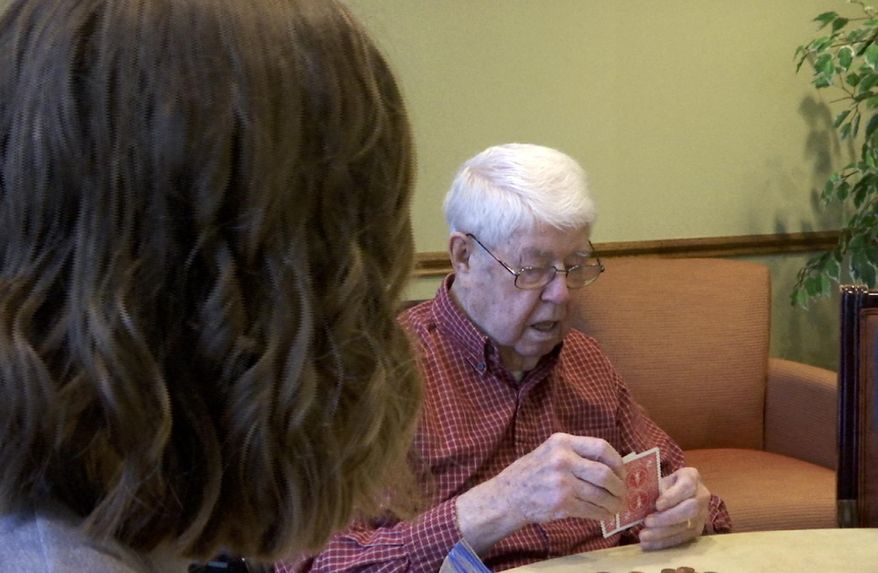 In this Jan. 18, 2017, image made from a video, David Burkholder looks at his cards during a poker game at the Clark on Keller Lake retirement home in Grand Rapids, Mich. Sitting next to Burkholder is Colette Chapp, who, along with two other Western Michigan University graduate students, are about a third of the way through the 19 months they will spend alongside 80 senior citizens at Clark on Keller Lake as part of what is believed to be one of the first such research projects of its kind in the U.S. Burkholder and Chapp have become friends. (AP Photo/Mike Householder)